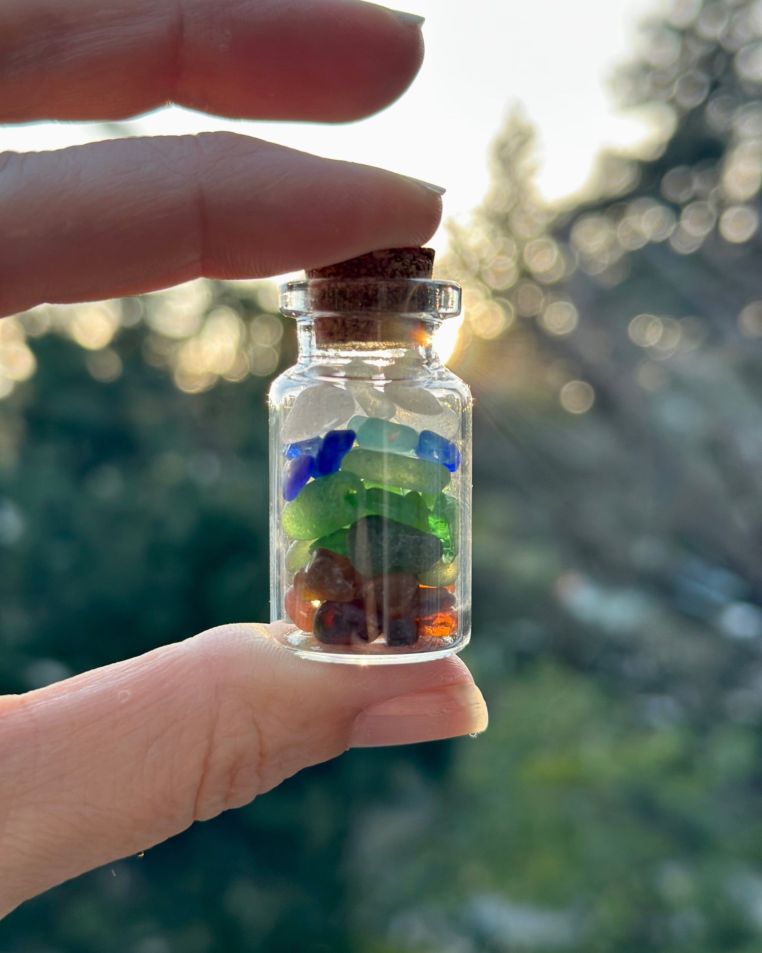 Glass bottle with colorful stones held by a hand against a blurred natural background